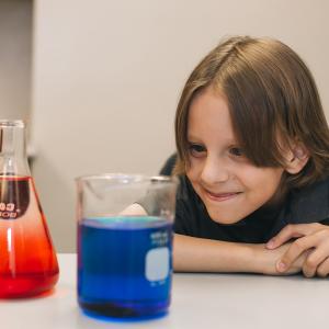 A young boy looking at science beakers filled with colored liquid 