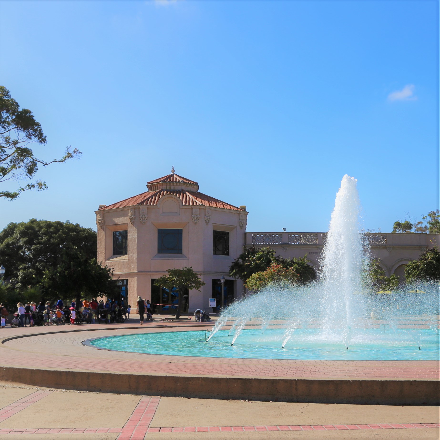 Fleet Science Center building entrance with water fountain and a line of people waiting to go into the building