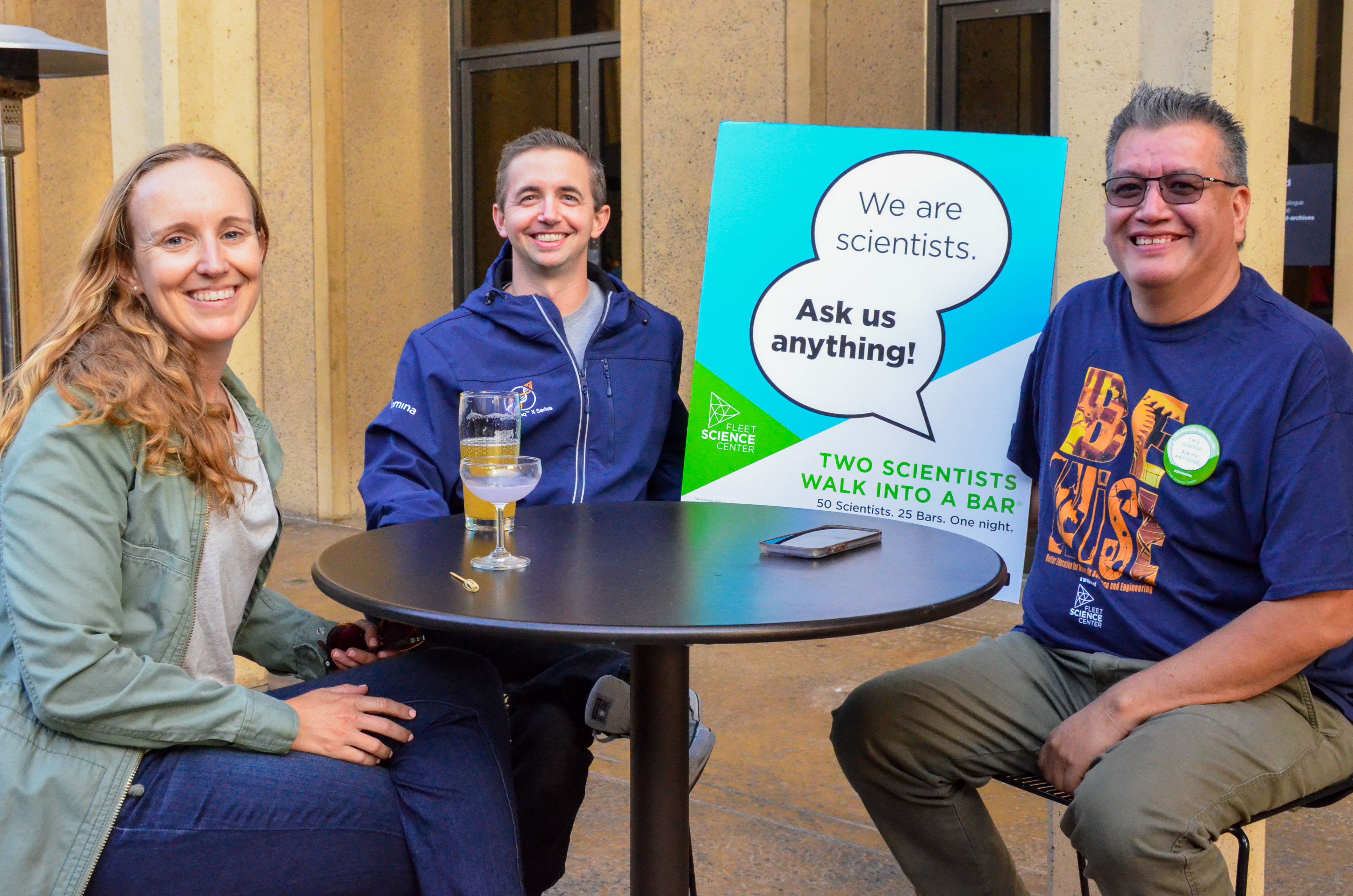 Three STEM professionals sitting at a table with a sign that reads "I'm a scientist. Ask me anything."