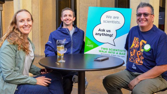 Three STEM professionals sitting at a table with a sign that reads "I'm a scientist. Ask me anything."