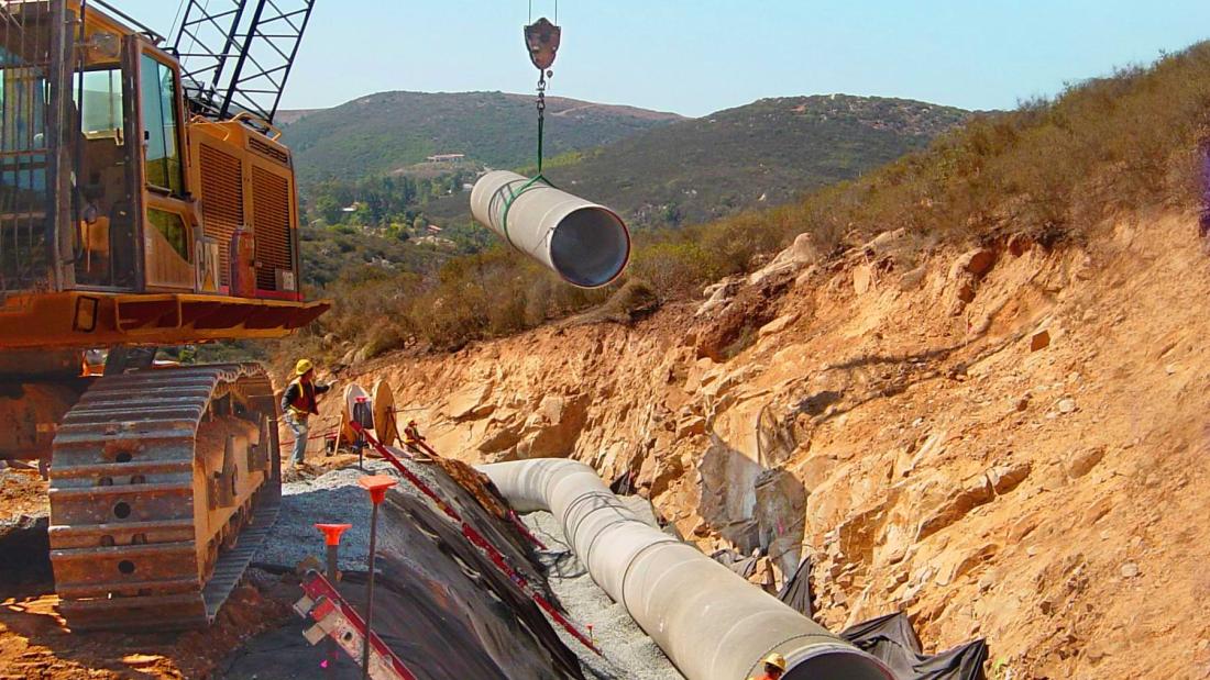 Crane lifting a large concrete pipe into a ditch in the desert