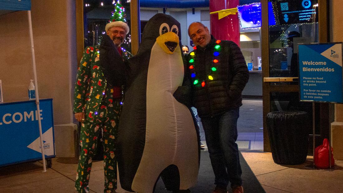 Two festive men on either side of a person wearing an inflatable penguin suit.