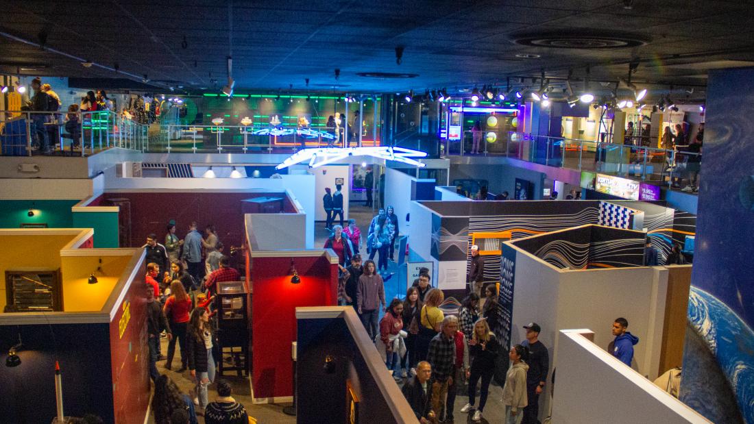 An aerial view of a science center with neon lights and many people walking through the spaces