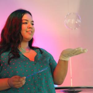 woman in a pink lit room holds out her hand while a larger bubble floats above 