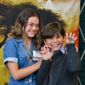 A girl and a boy pose in front of a safari background. The boy is holding up is hands and pretending to be a lion 