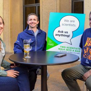 Three STEM professionals sitting at a table with a sign that reads "I'm a scientist. Ask me anything."