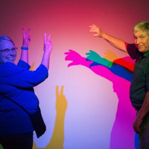 Two seniors making hand shadows on a violet and red colored wall